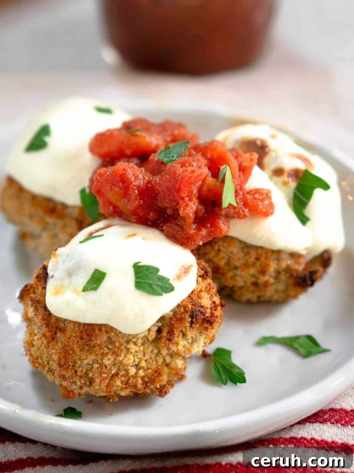 Sideview of three breaded chicken meatballs topped with melted parmesan cheese and fresh tomato marinara - Hostess At Heart