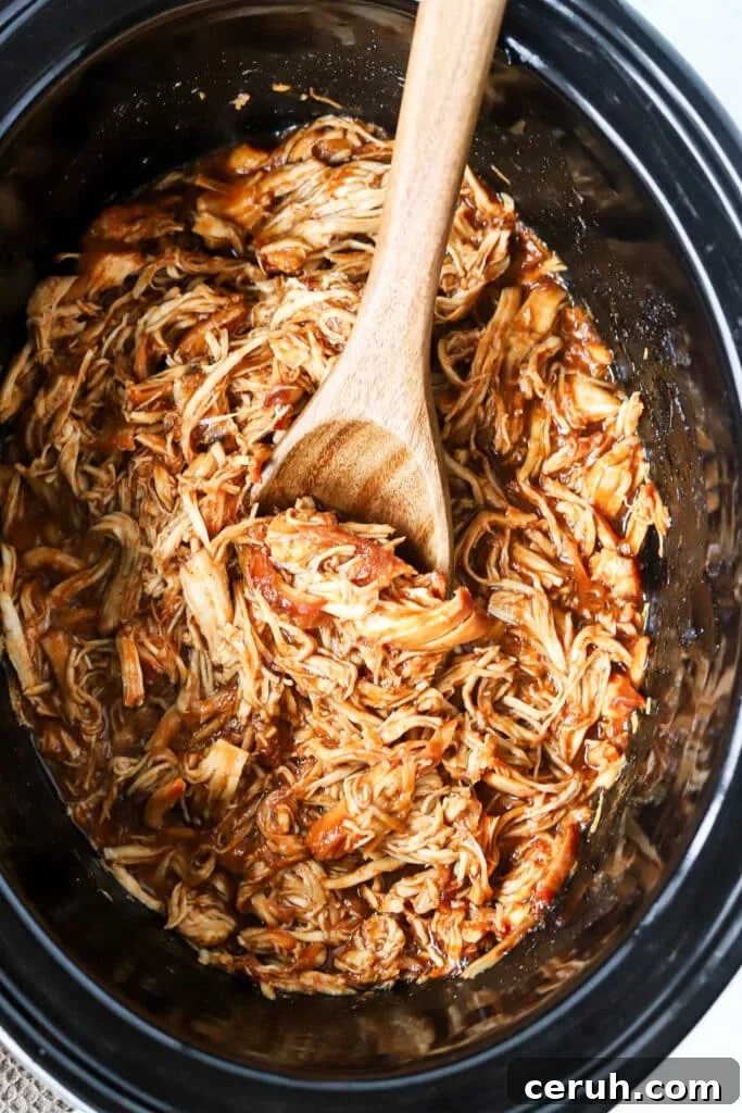 Brown sugar BBQ chicken in a slow cooker with a wooden spoon.