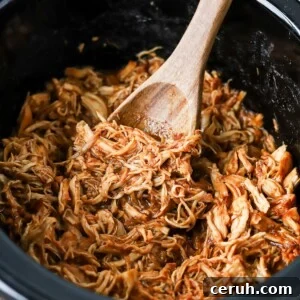 Brown sugar BBQ chicken in a slow cooker with a wooden spoon.