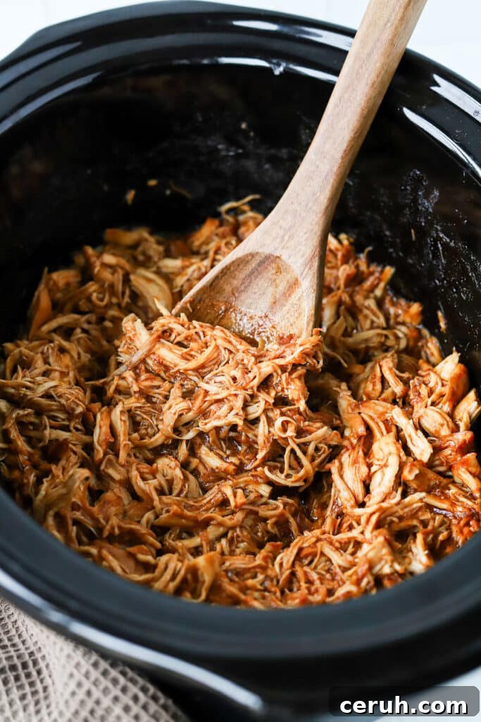 Brown sugar BBQ chicken in a slow cooker with a wooden spoon.