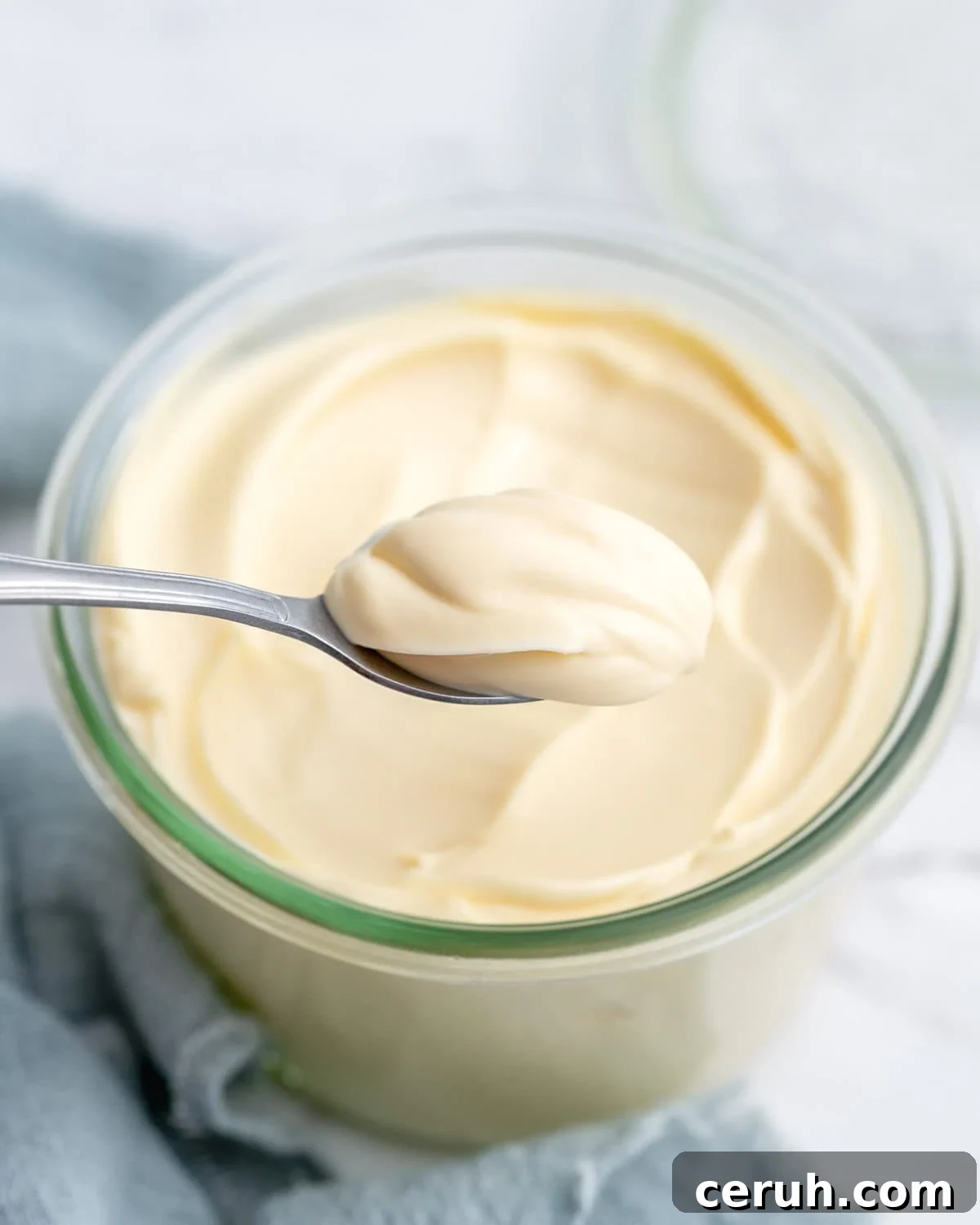Spoon lifting a generous dollop of creamy homemade mayonnaise from the jar, showing its thick, stable texture as it holds its shape.