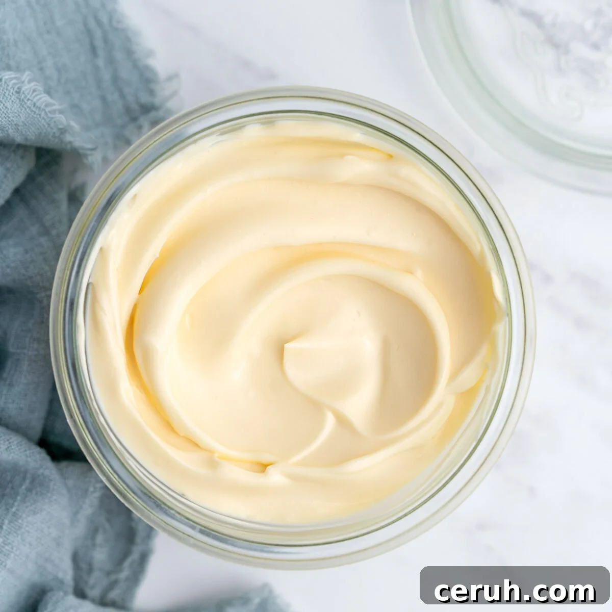 Completed homemade mayonnaise in an open glass jar, showing its glossy, pale yellow surface and creamy texture.