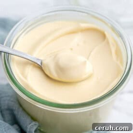 Spoon lifting a generous dollop of creamy homemade mayonnaise from a jar.