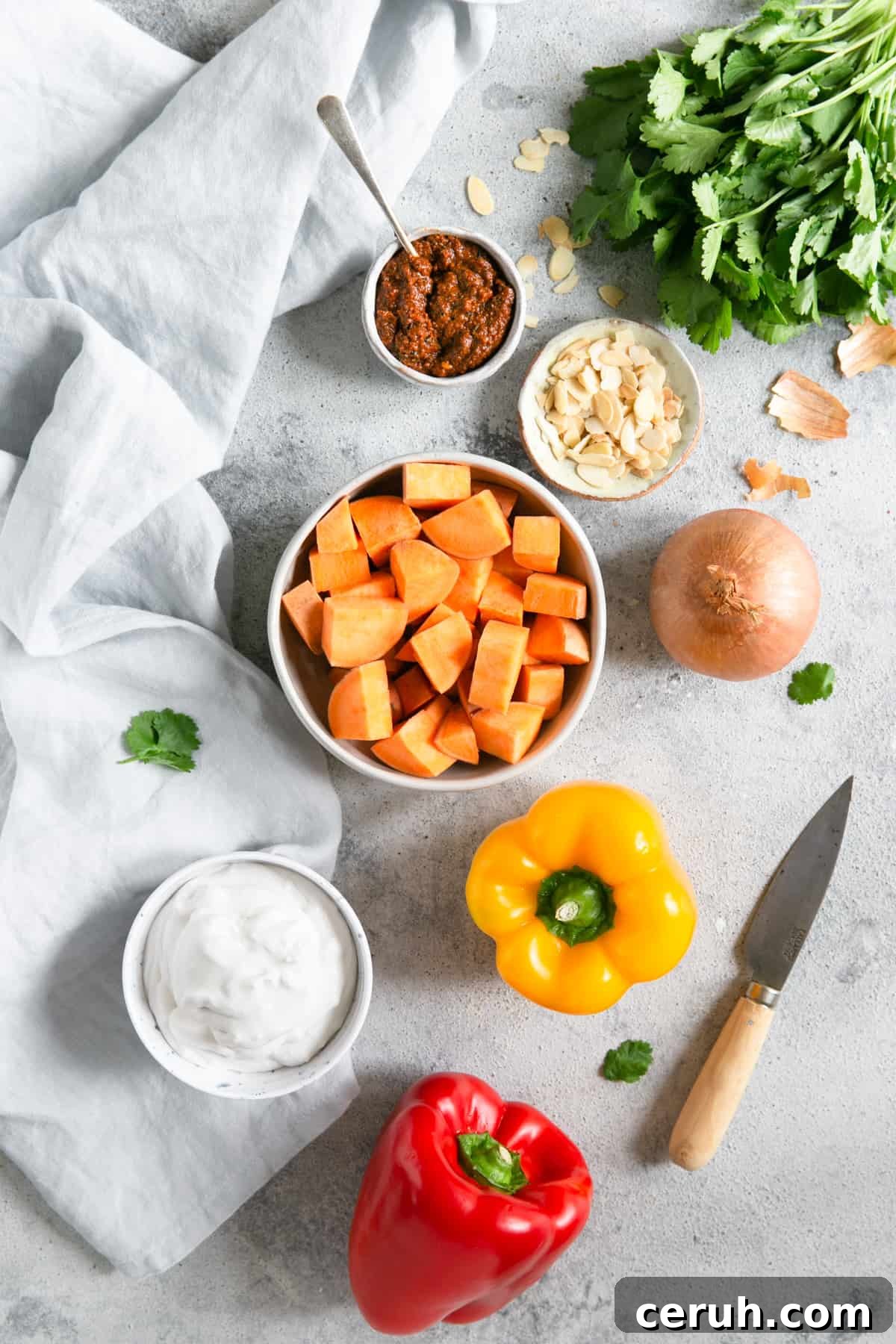 overhead shot of the ingredients for sweet potato curry; peppers, coconut milk, sweet potato, onion, toasted almonds, coriander, curry paste