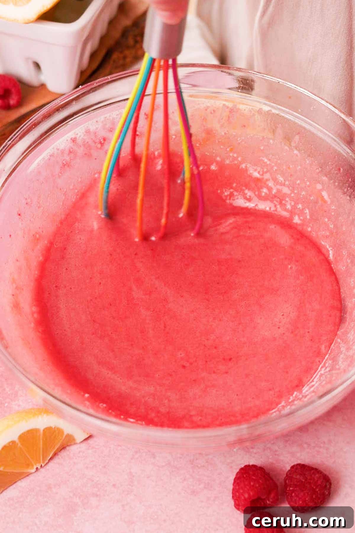 stirring creamy filling for raspberry bars in a large glass bowl with a whisk