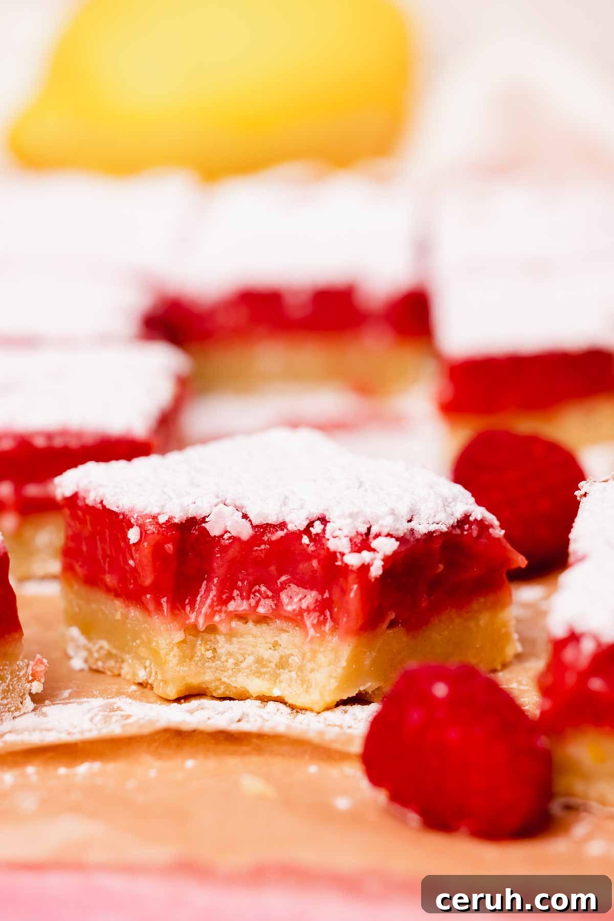 lemon raspberry bar with a bite taken out of it on parchment paper with fresh raspberries