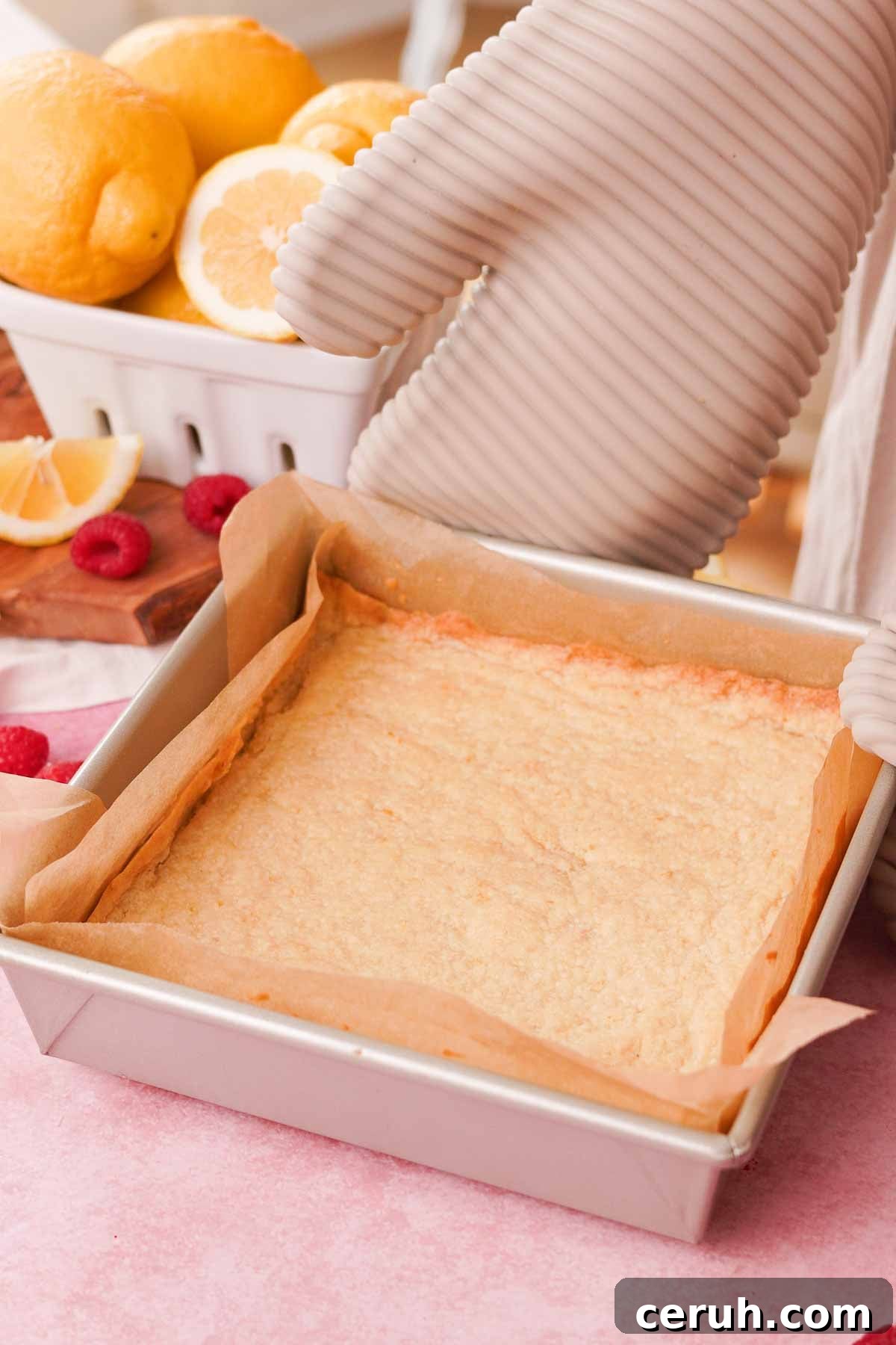 baked shortbread crust for lemon raspberry bars in parchment lined square baking pan
