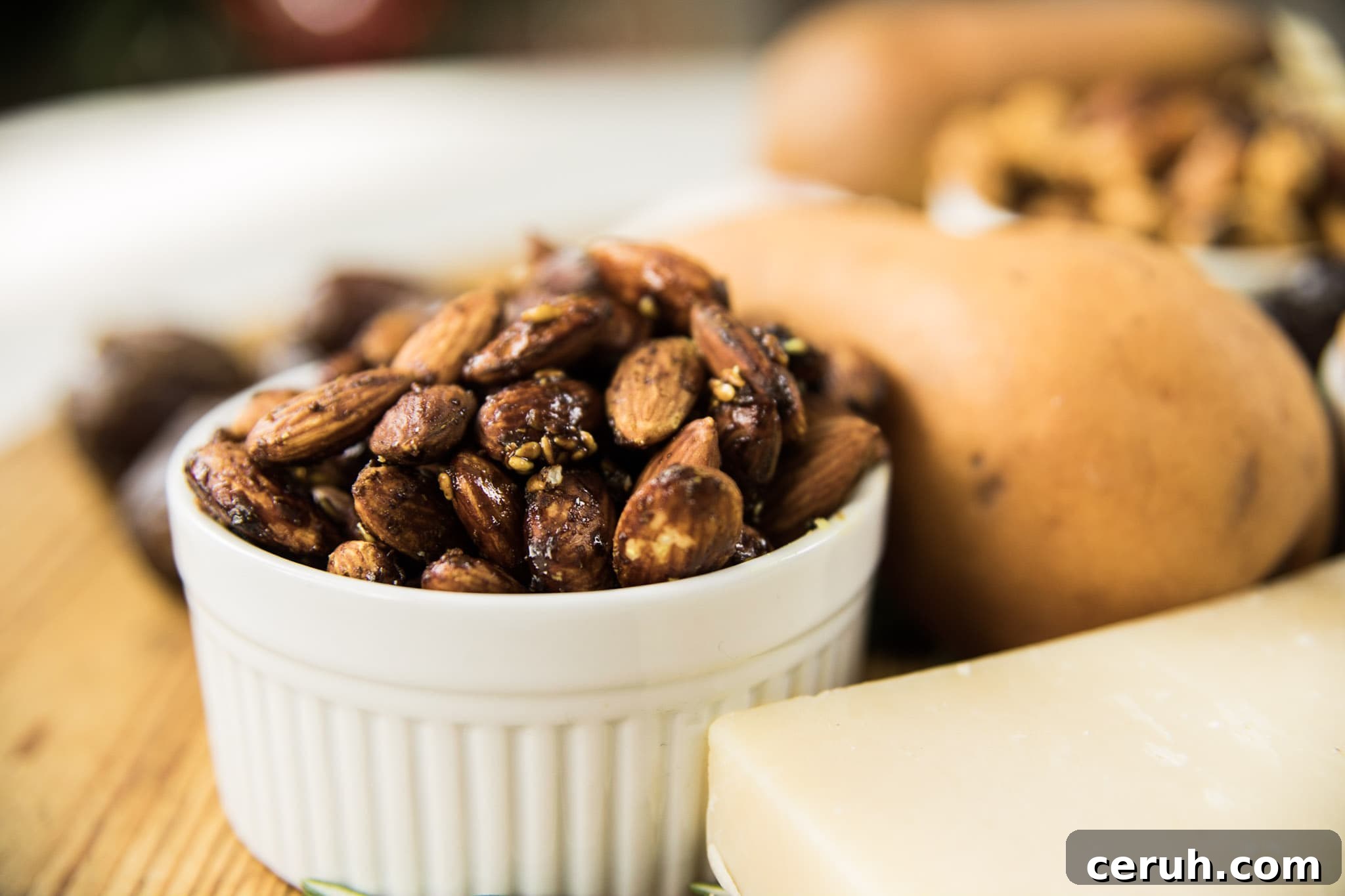 White bowl filled with toasted almonds with pear and hunk of cheese around all on wooden board