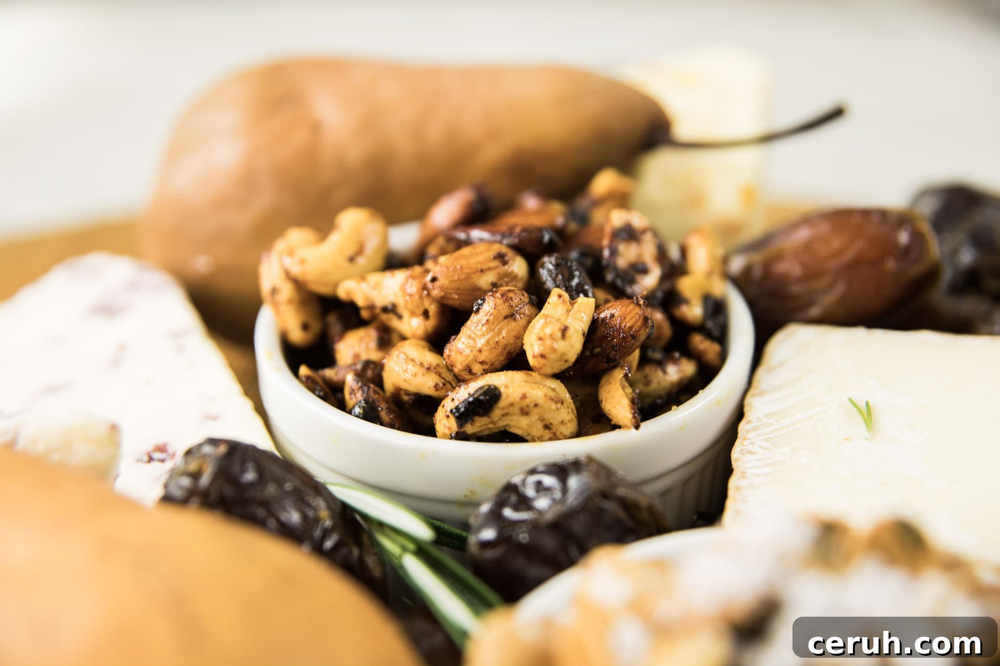 White bowl filled with mixed nuts with pears, dates, and cheese all around on white surface