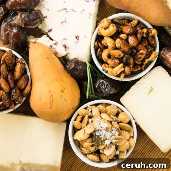 Top down view of three spiced nuts sitting on wood board with chunks of cheese, pears, and dates all around