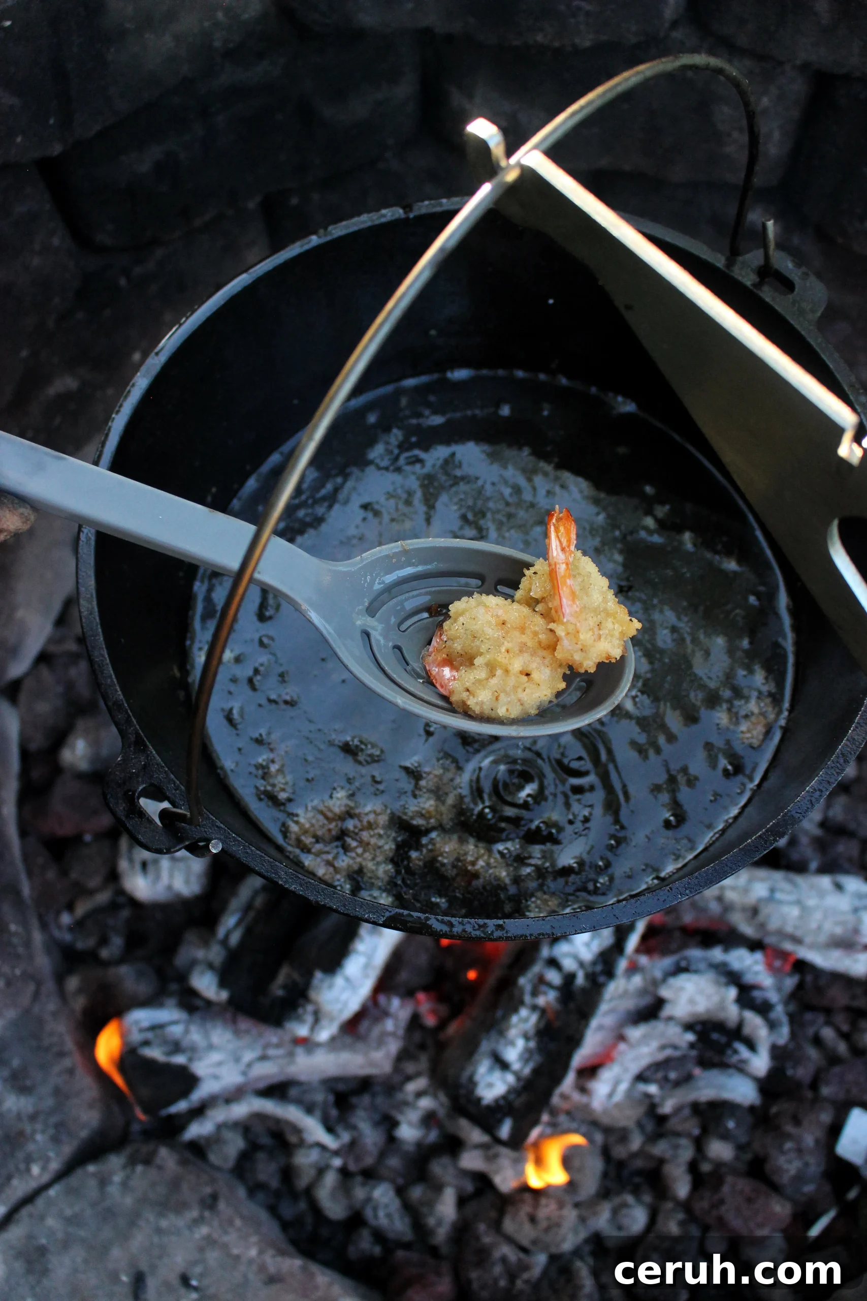 Pulling two fried shrimp from the dutch oven.