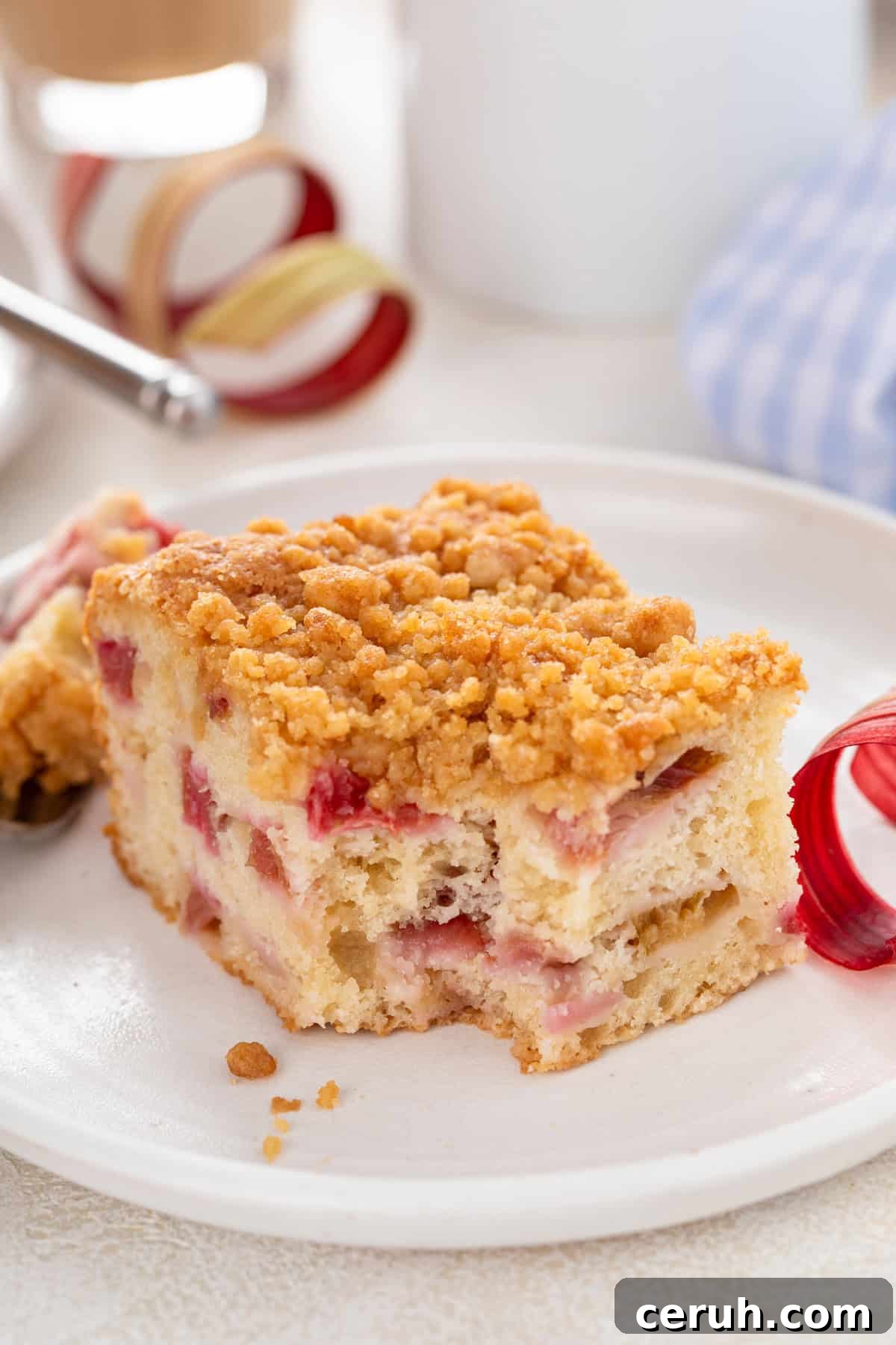 Bite taken from the corner of a piece of rhubarb streusel cake on a white plate.