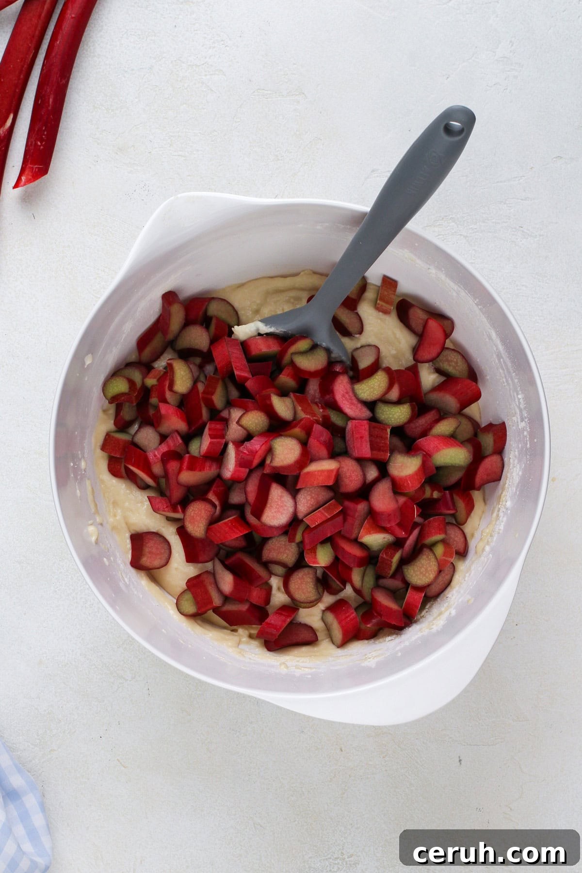 Sliced rhubarb added to a white bowl with cake batter.