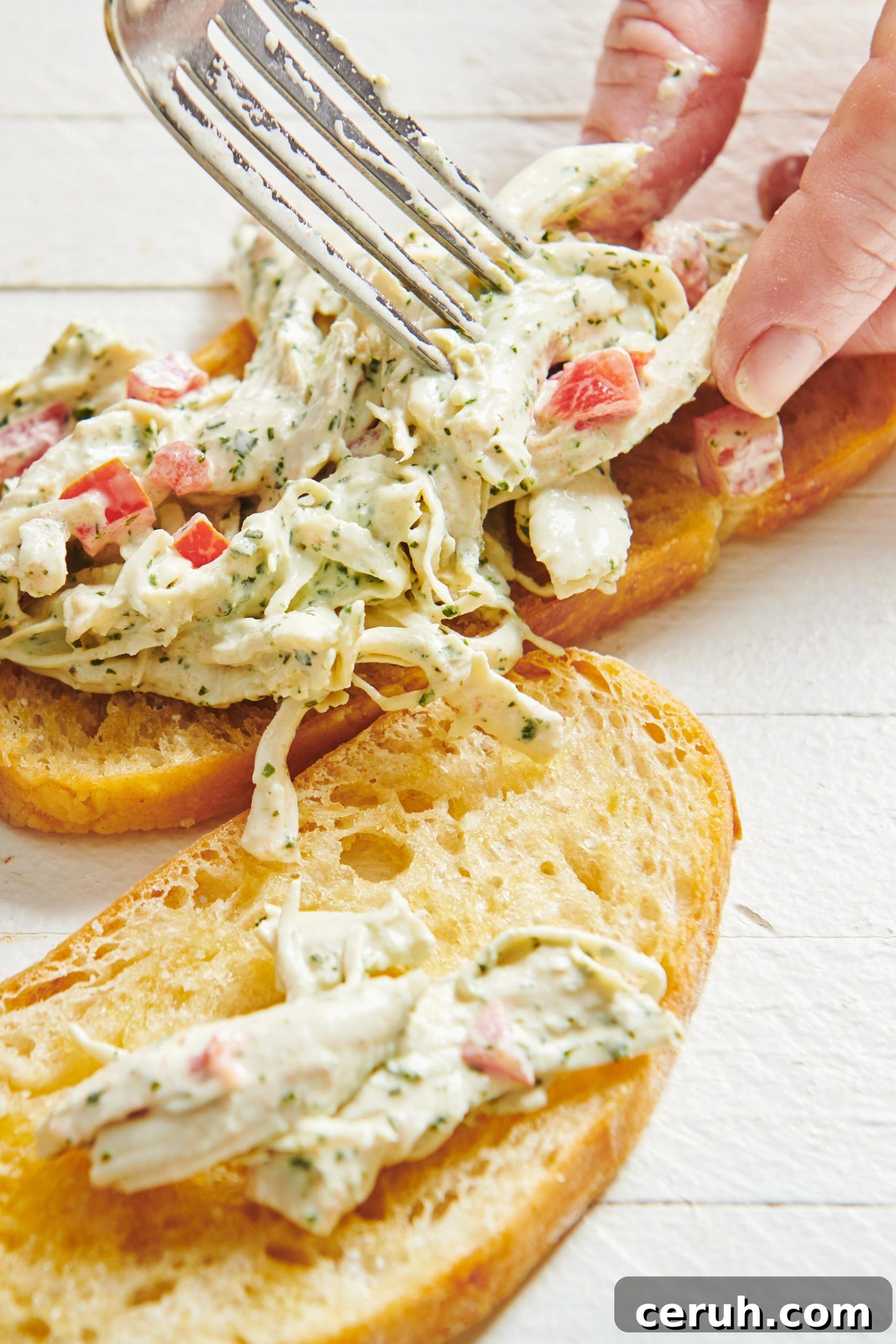 Spreading Herbed Chicken Salad onto toasted bruschetta with fork.