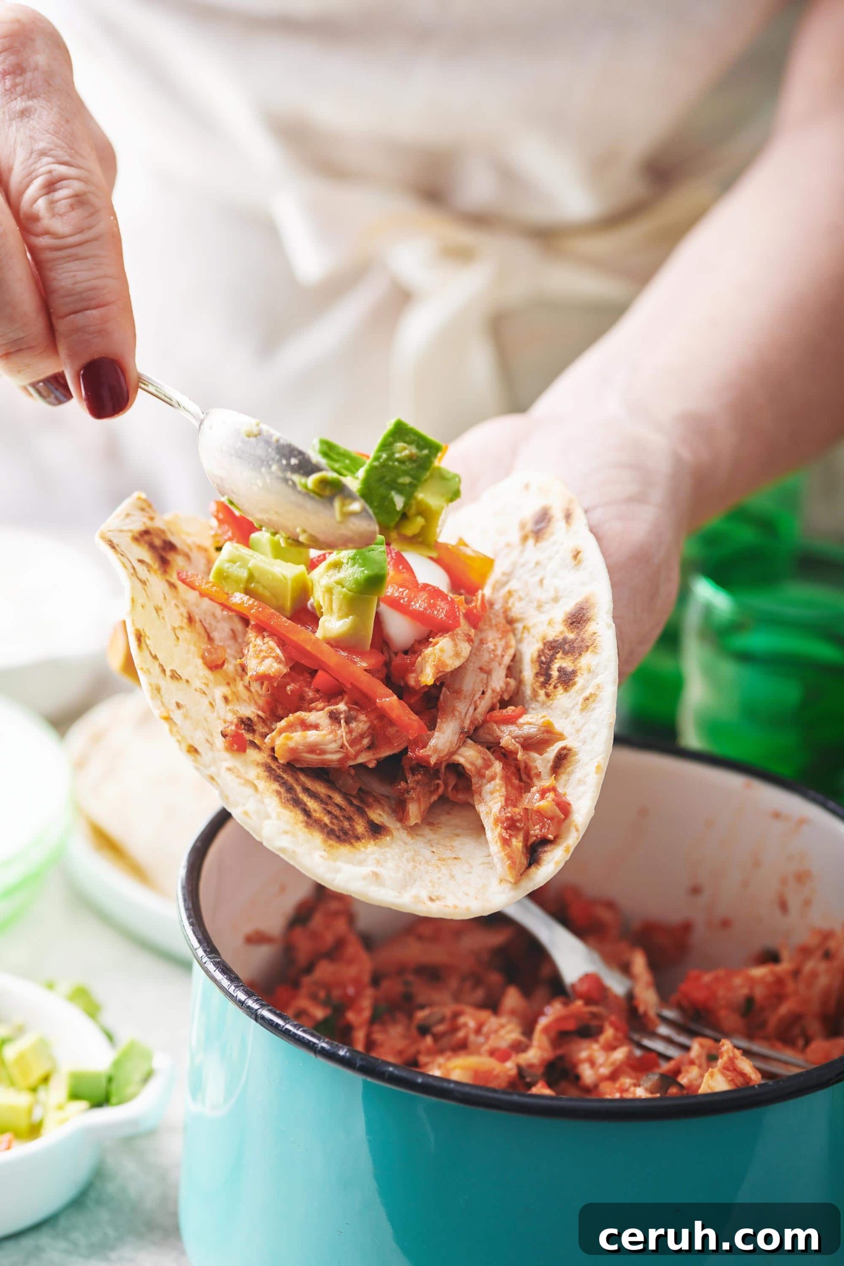 Spoon scooping avocado onto a Shredded Chicken Taco.