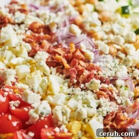 Late Summer Cobb Salad topped with bacon, red onion, crumbled cheese, and other toppings.