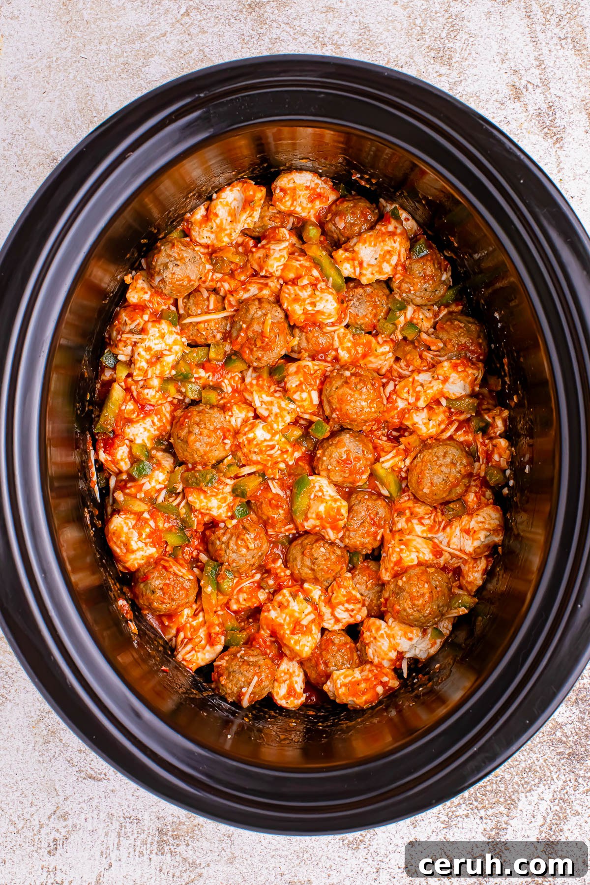 A slow cooker filled with a mixture of rice, meatballs, diced vegetables, and a red sauce.