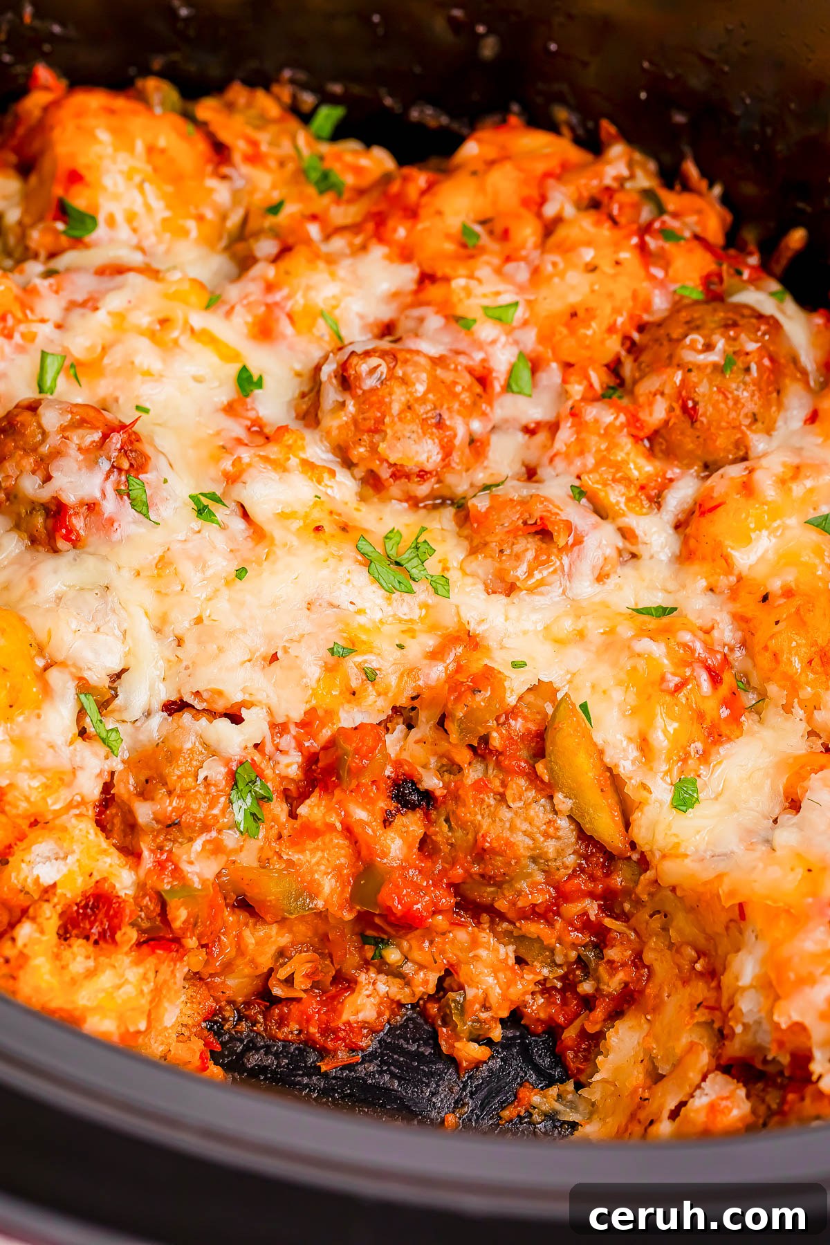 A close-up of a baked casserole with meatballs, pasta, melted cheese, and garnished with herbs.