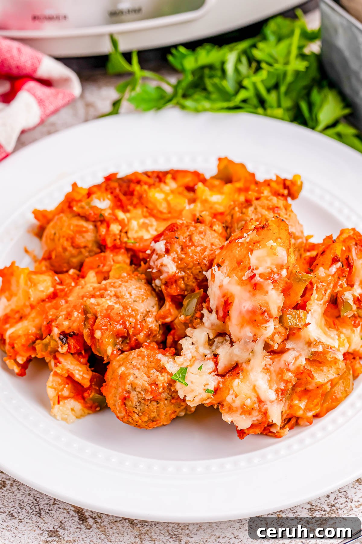 Plate of cheesy baked meatballs with tomato sauce, topped with melted cheese and garnished with herbs.