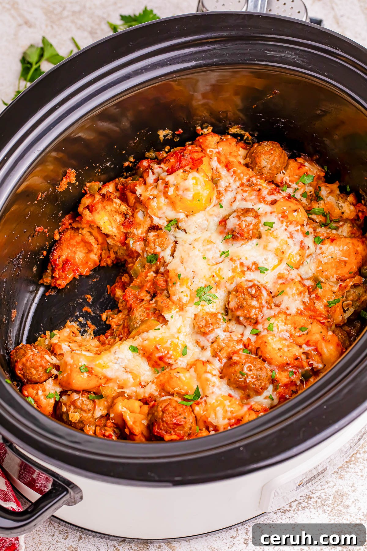 Cheesy meatballs and pasta dish in a slow cooker, topped with herbs.