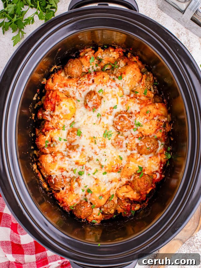 A slow cooker containing meatballs in a tomato sauce, topped with melted cheese and garnished with chopped herbs.