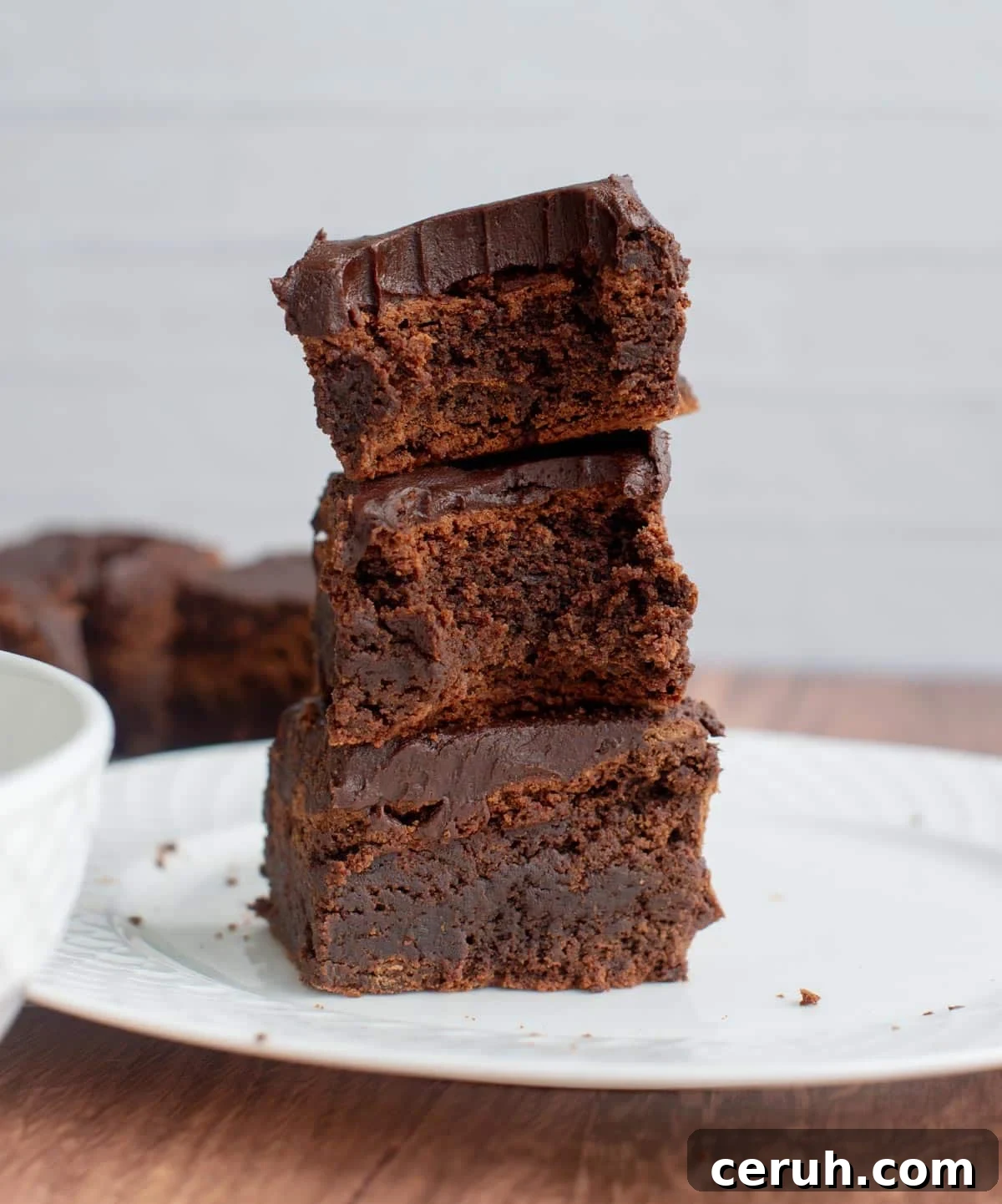 A stack of three sourdough brownies on a plate with a bite taken out of them.