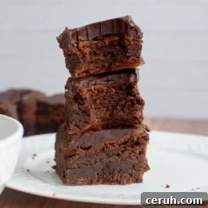 A stack of three sourdough brownies on a plate with a bite taken out of them.