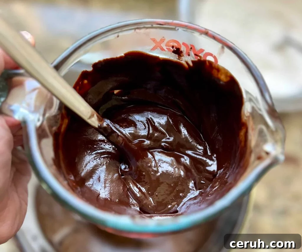 A liquid measuring cup contains a chocolate mixture with a spoon sticking out of it.