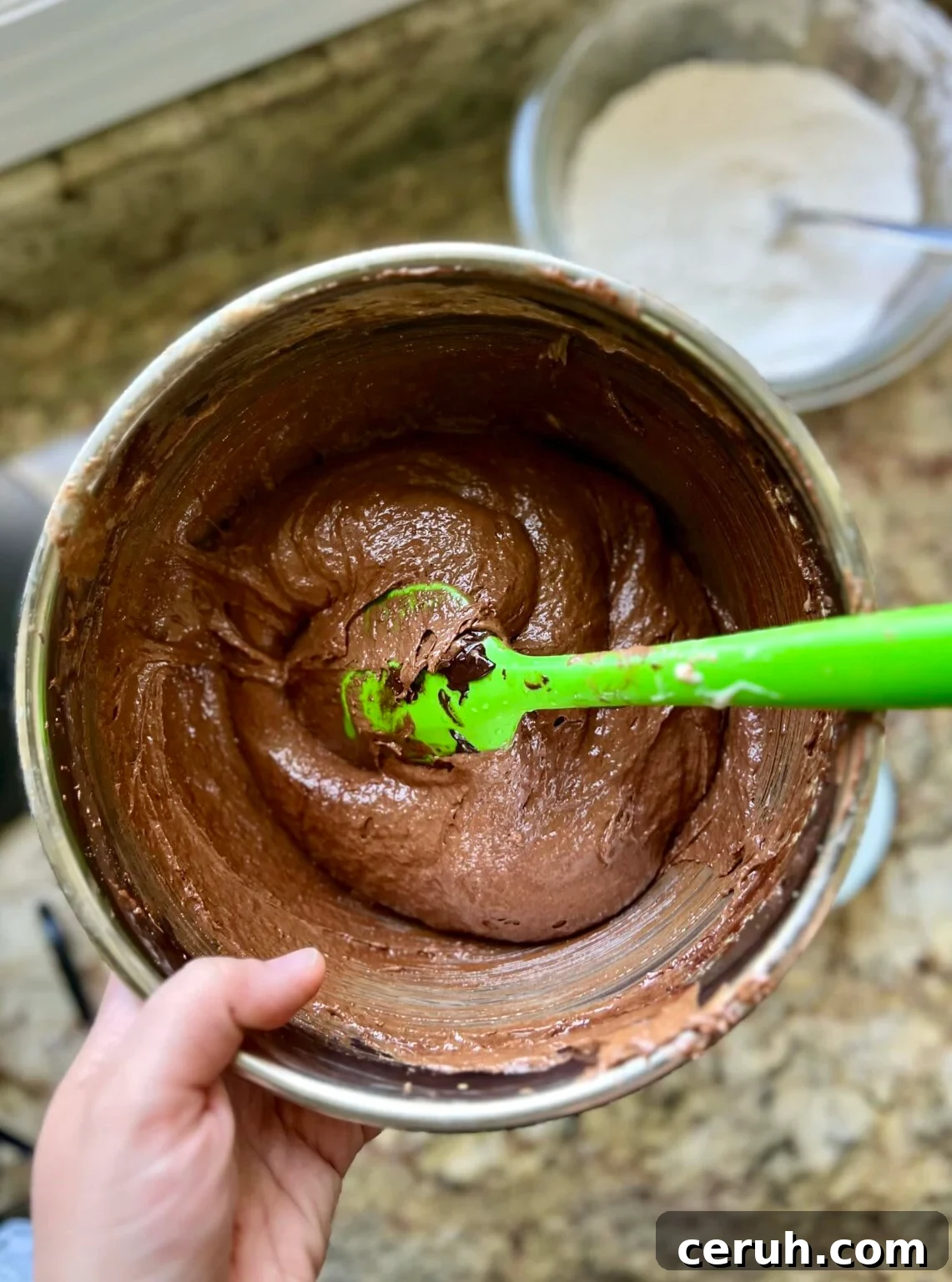 A spatula sits in a mixing bowl filled with brownie batter.