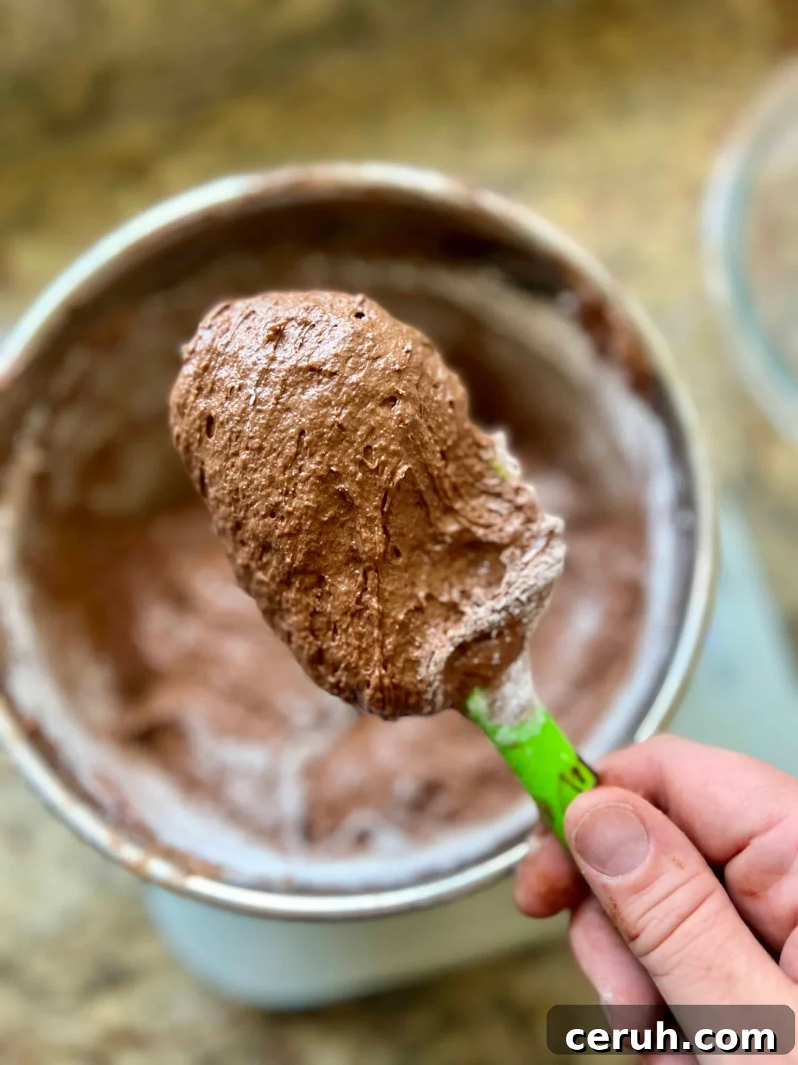 A spatula holds brownie batter over a mixing bowl filled with the remaining batter.