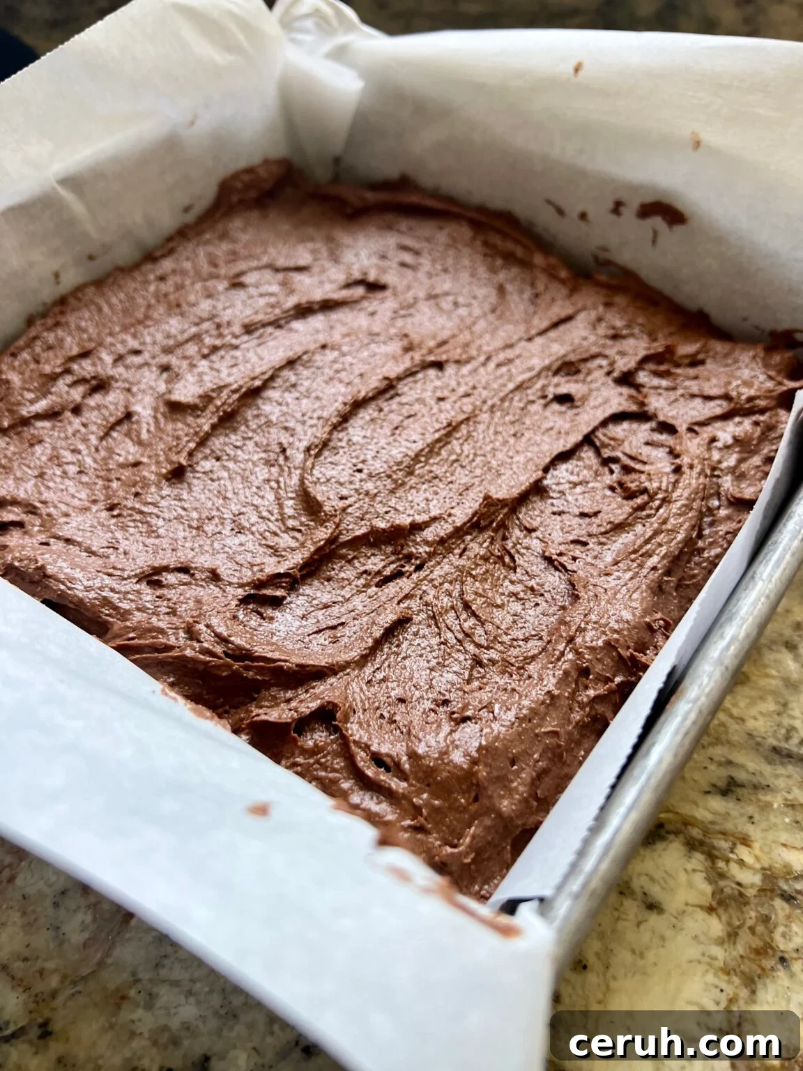 A square baking pan is lined with parchment paper and filled with brownie batter.