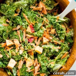 A wooden salad bowl filled with a kale apple salad with a serving spoon in it.