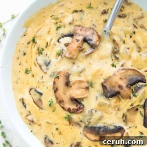 A bowl of vegan cream of mushroom soup with a spoon in it and topped with cooked mushrooms.