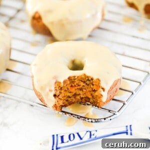 A carrot cake donut with icing on it with a bite out of it.