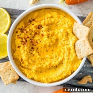 A bowl of carrot dip topped with chili flakes and two crackers.