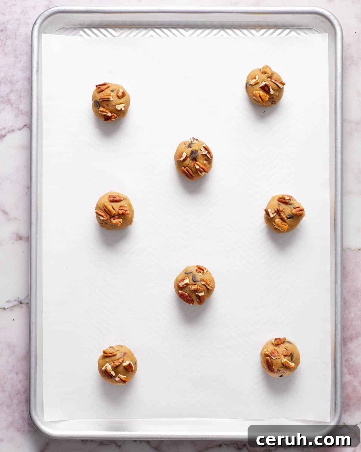 Chocolate Chip and Pecan Cookies — Chewy Oven-Baked Recipe 5 Cookie dough rolled into balls and arranged on a parchment paper lined baking sheet.