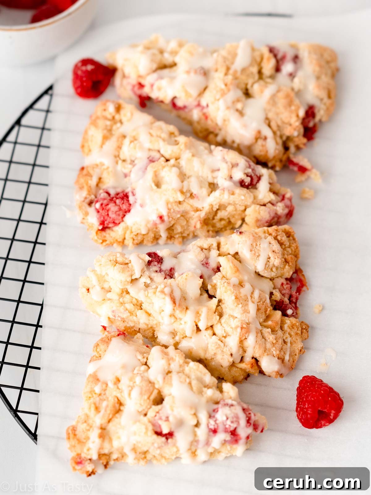 Four glazed white chocolate raspberry scones on parchment paper.