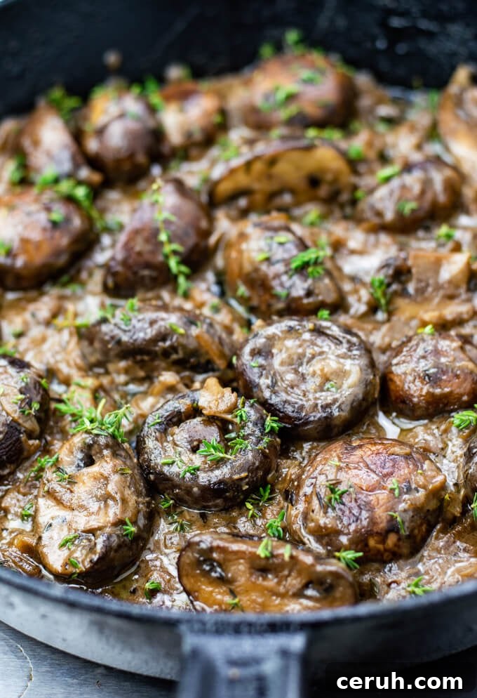 A close-up photo of sautéed mushrooms in a creamy sauce with chopped thyme sprinkled on top. All of this is in a cast iron skillet.