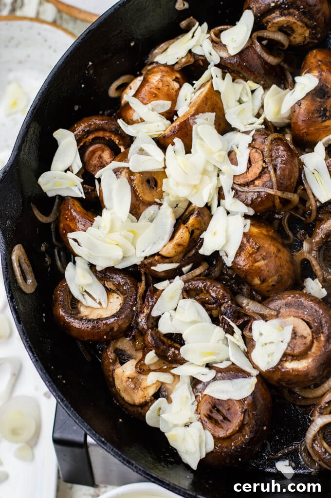 A cast iron skillet of sautéed mushrooms with sliced garlic sitting on top of the mushrooms.