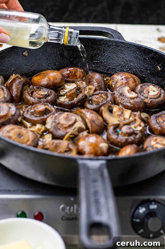 Sautéed mushrooms are in a cast iron skillet with a bottle of wine being poured into the mushrooms. 