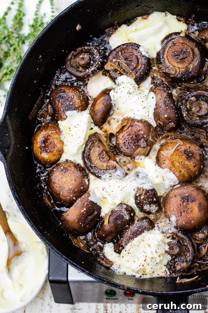Sautéed mushrooms sit in a cast iron skillet with dollops of mascarpone cheese. 