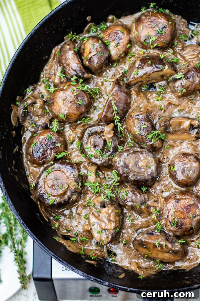 A close-up photo of sautéed mushrooms in a creamy sauce with chopped thyme sprinkled on top. All of this is in a cast iron skillet.