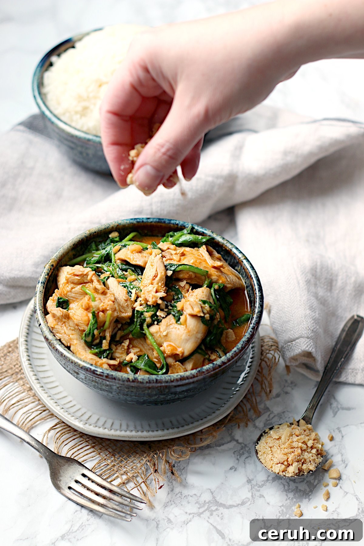 Thai Rama Chicken in Creamy Peanut Sauce Recipe 2 A hand sprinkling chopped peanuts into a bowl of Thai Swimming Rama Chicken.