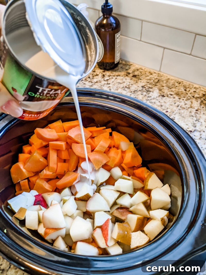 Savory Carrot and Pear Soup Recipe for Cozy Weeknights 4 A hand pouring in the coconut milk into a slow cooker with cubed carrots and pears
