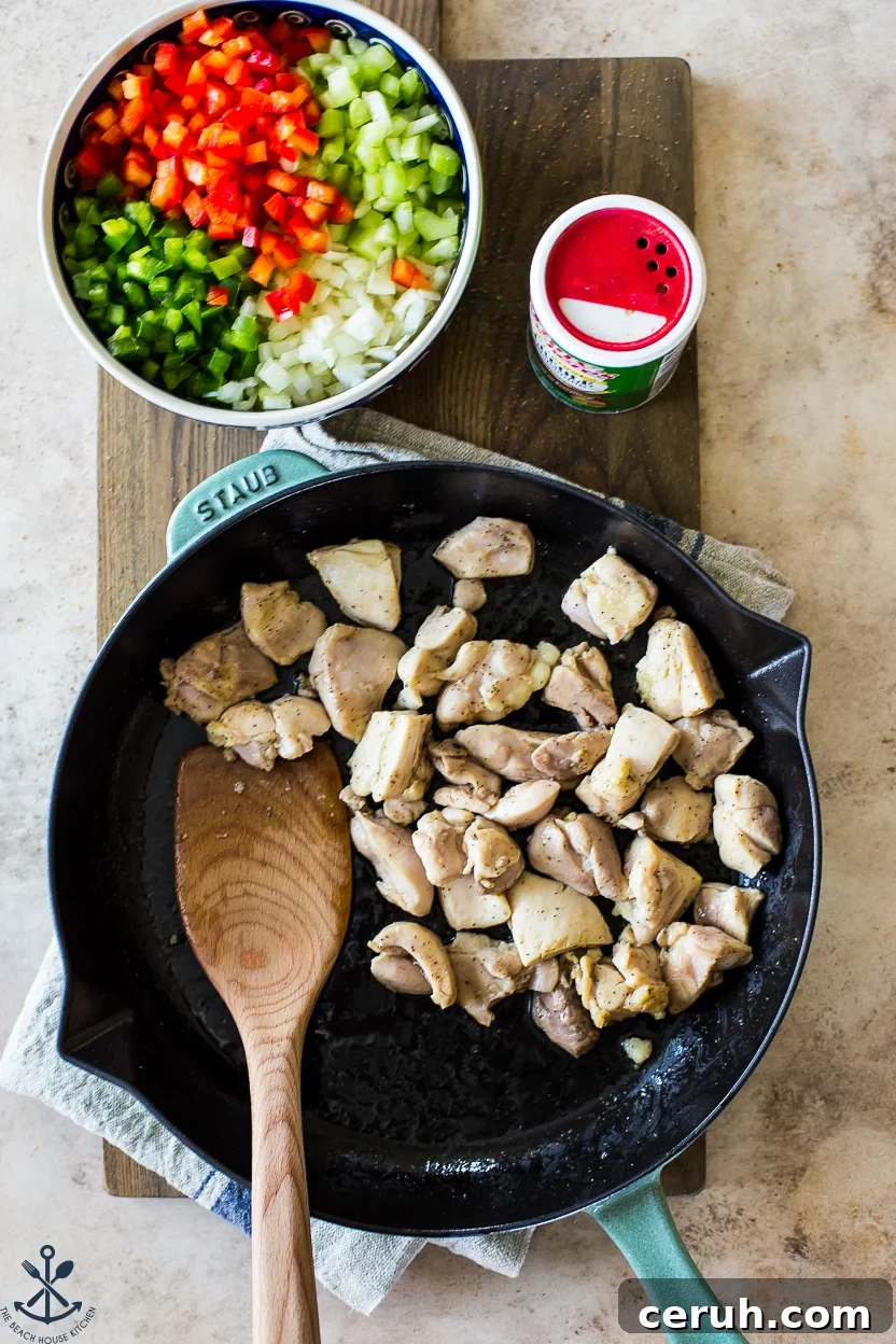 Overhead photo of a skillet of cooked chicken with a cowl of onions, peppers and celery off to the side