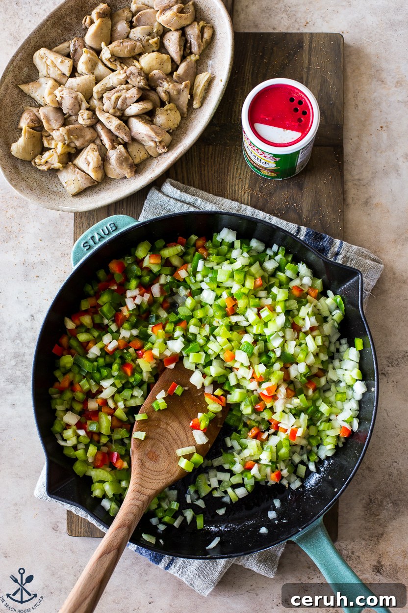 Overhead photo of a skillet of onions, peppers and celery with a plate of cooked chicken off to the side