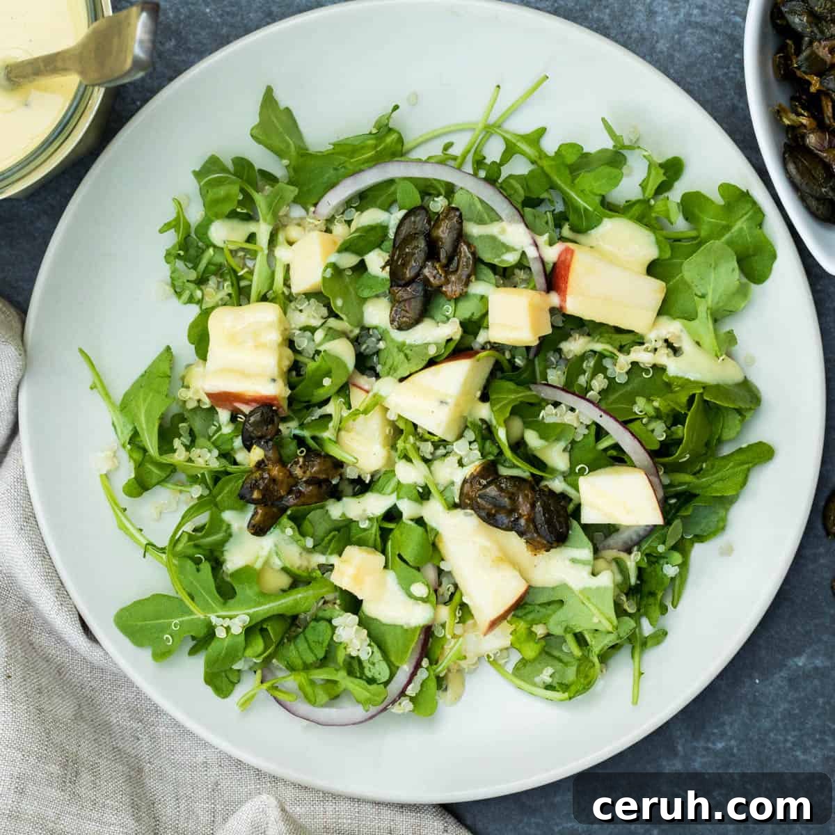 plate of arugula salad with apples, quinoa, red onion, cheddar cheese, and honey mustard dressing