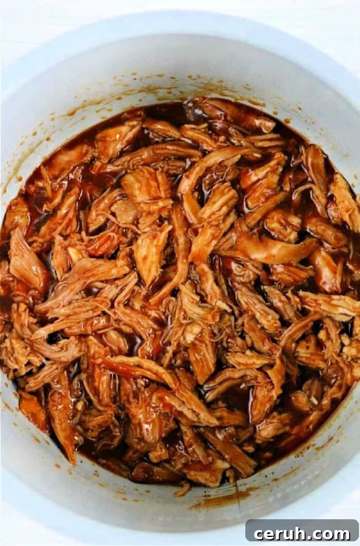 Shredded barbecue pork in a white pot, covered in rich, dark sauce, reminiscent of those delicious leftover pork loin recipes.
