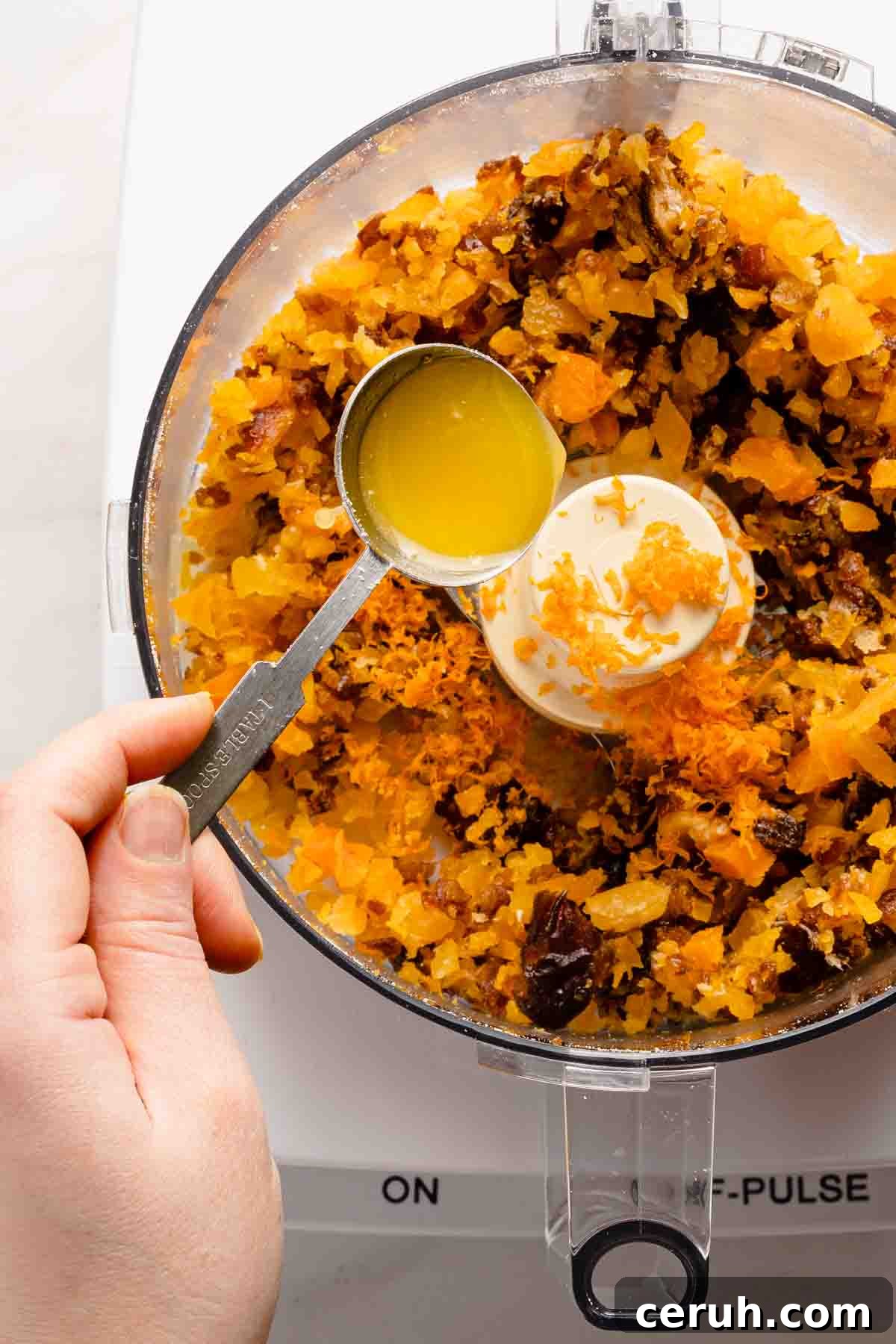 spoon of orange juice being added to fruit in food processor.