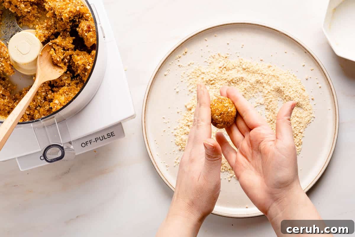 hands rolling bliss ball mixture into ball overtop plate with ground cashews on it
